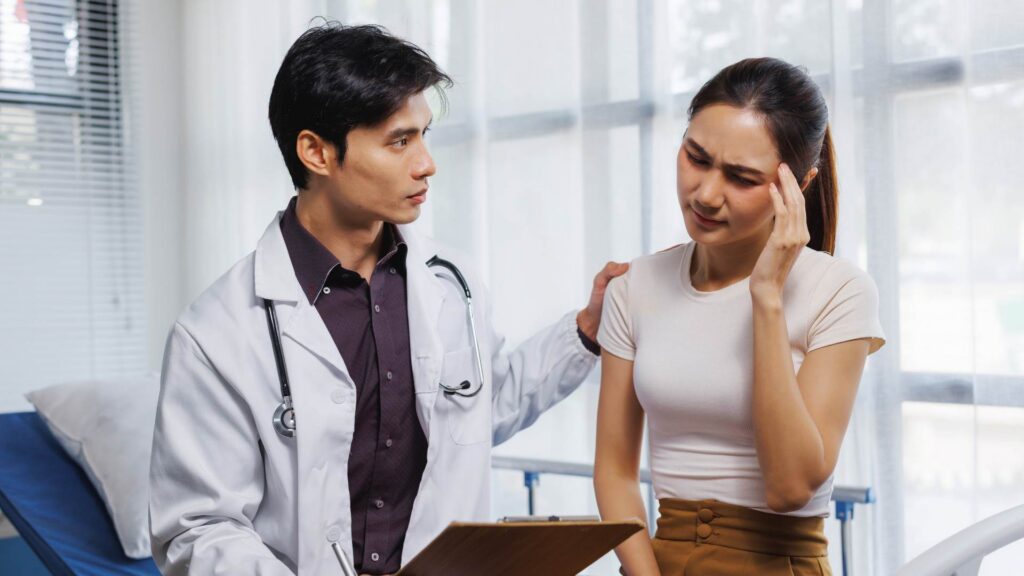 Patient holding their head in discomfort while a doctor offers support for sobriety fatigue.